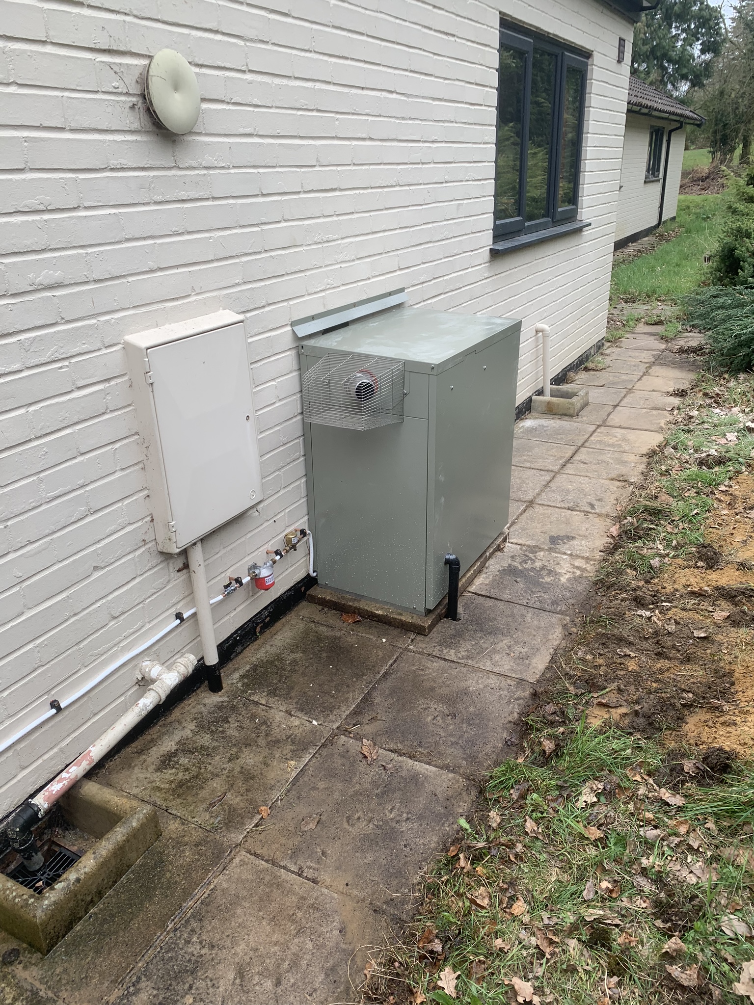 Outdoor oil boiler beside a white weatherboard bungalow