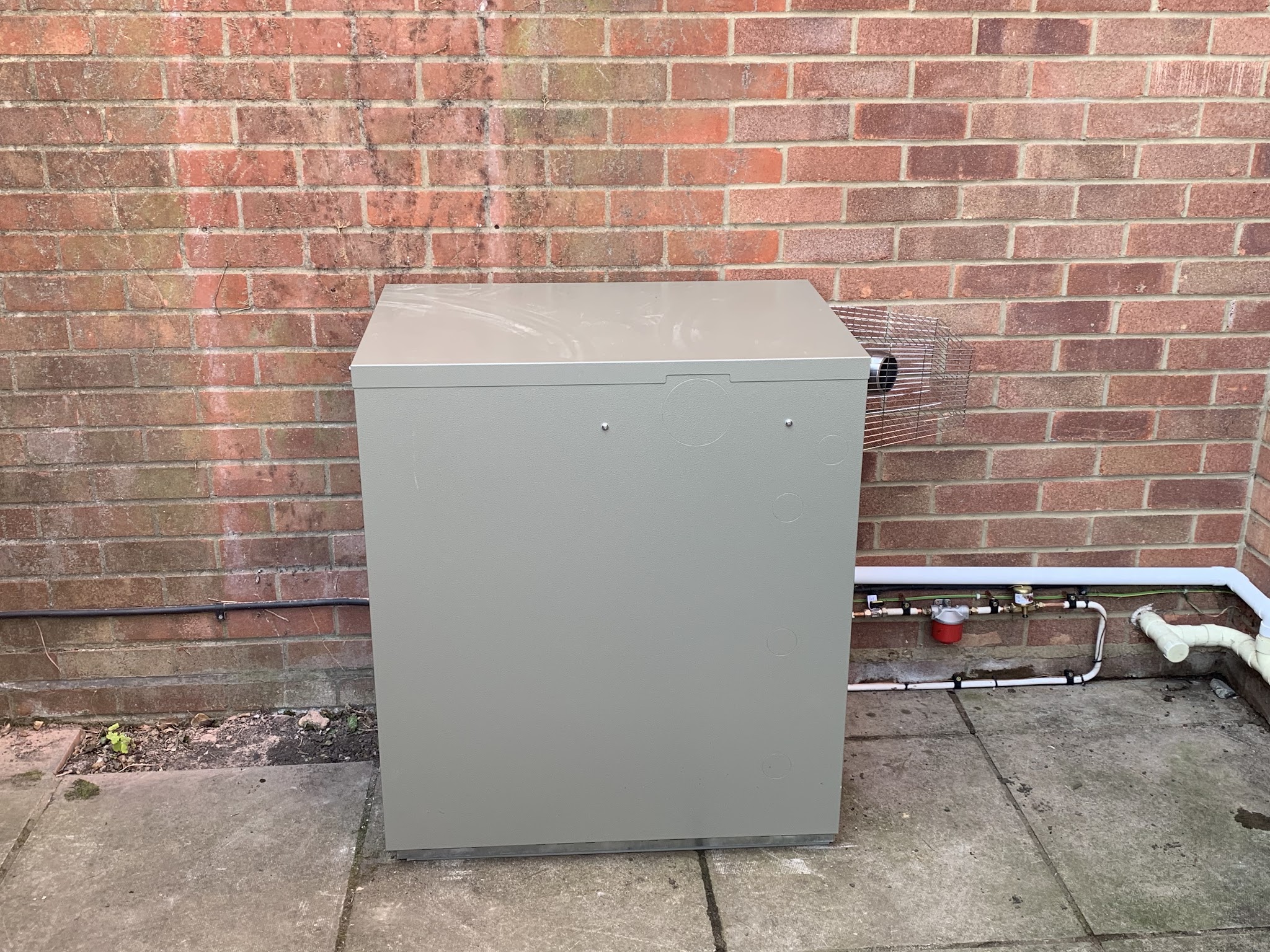 Outdoor oil boiler installed against a brick wall with neat pipe runs